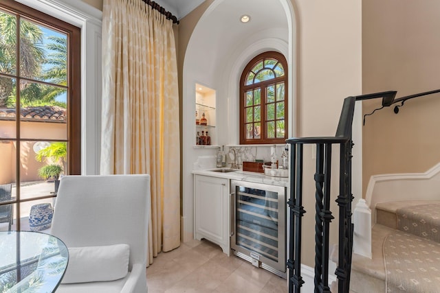 bar featuring beverage cooler, plenty of natural light, sink, and white cabinetry