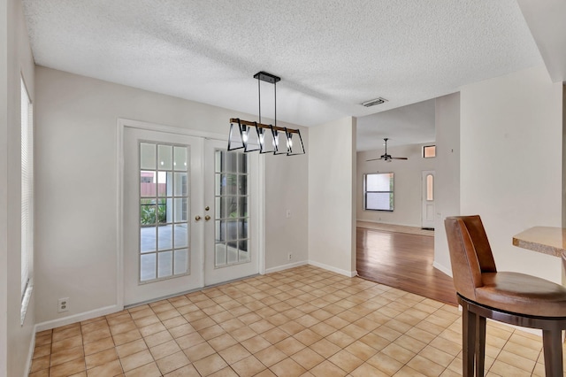 unfurnished dining area featuring ceiling fan, a textured ceiling, french doors, and light tile patterned flooring