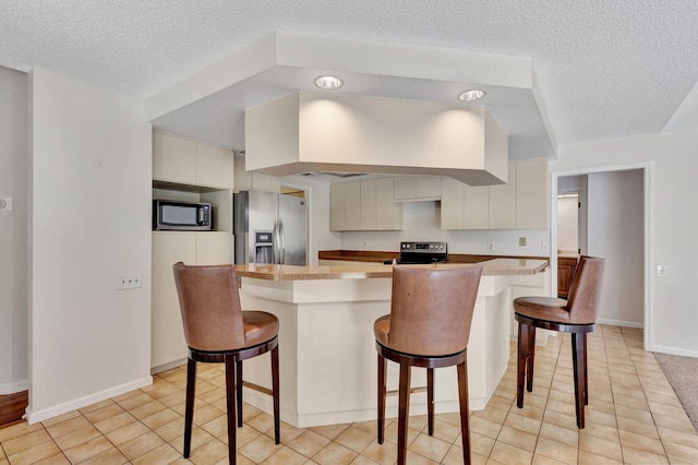 kitchen featuring stainless steel appliances, a textured ceiling, a kitchen bar, and light tile patterned floors