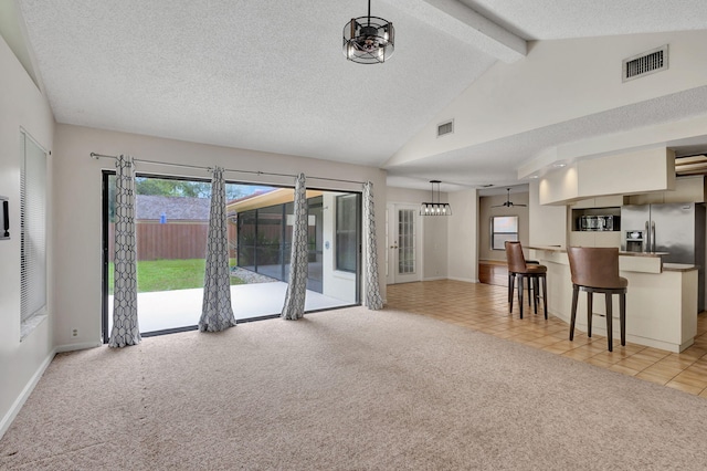 unfurnished living room with light carpet, a textured ceiling, lofted ceiling with beams, and an inviting chandelier