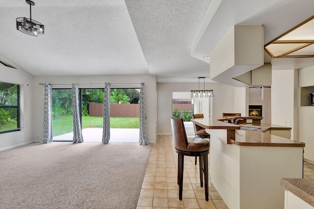 kitchen with a textured ceiling, a breakfast bar area, sink, light tile patterned floors, and decorative light fixtures