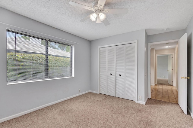 unfurnished bedroom featuring ceiling fan, light colored carpet, a textured ceiling, and a closet