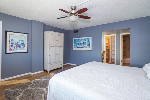 bedroom with ceiling fan, connected bathroom, a textured ceiling, a walk in closet, and hardwood / wood-style floors