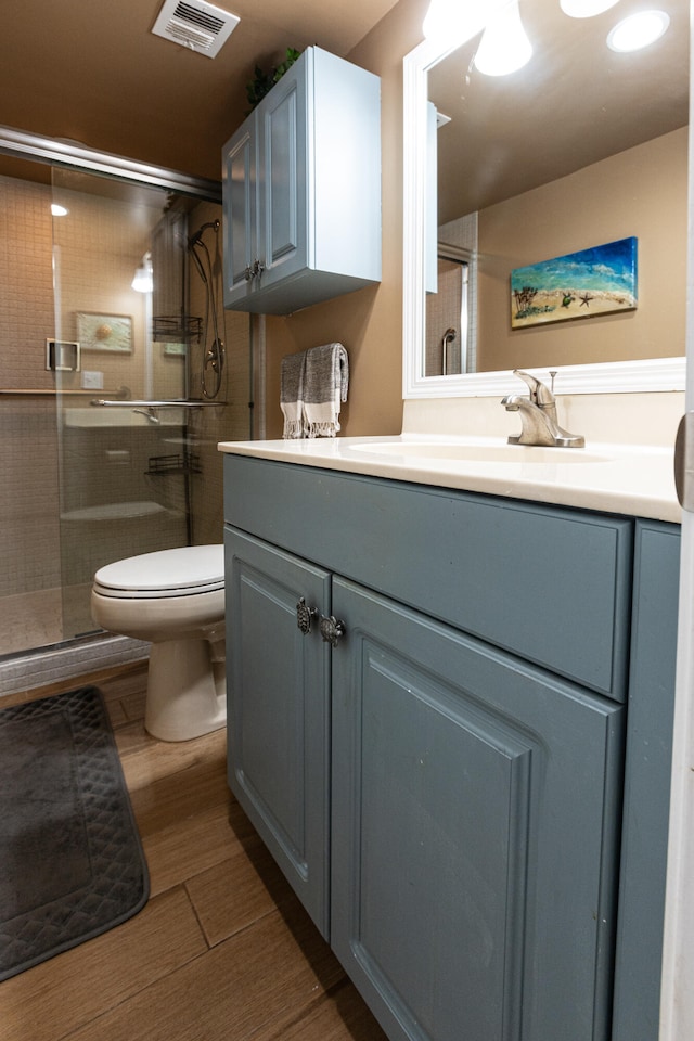 bathroom with hardwood / wood-style floors, vanity, a shower with shower door, and toilet