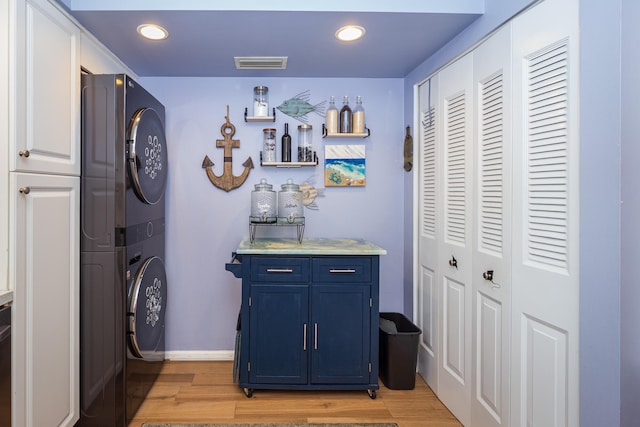 bar with blue cabinetry, light wood-type flooring, and stacked washer / dryer