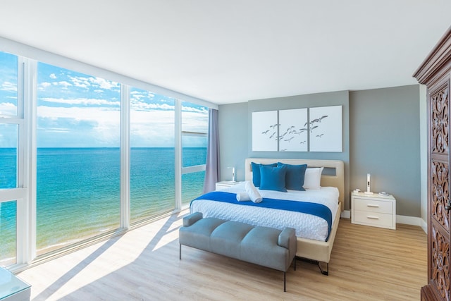 bedroom with expansive windows, a water view, a view of the beach, and light wood-type flooring