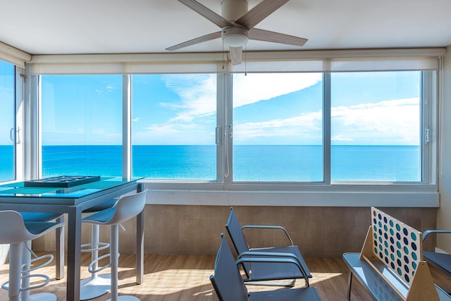 sunroom with ceiling fan and a water view