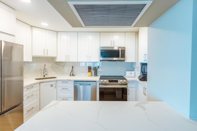 kitchen featuring white cabinetry, sink, light stone counters, backsplash, and appliances with stainless steel finishes