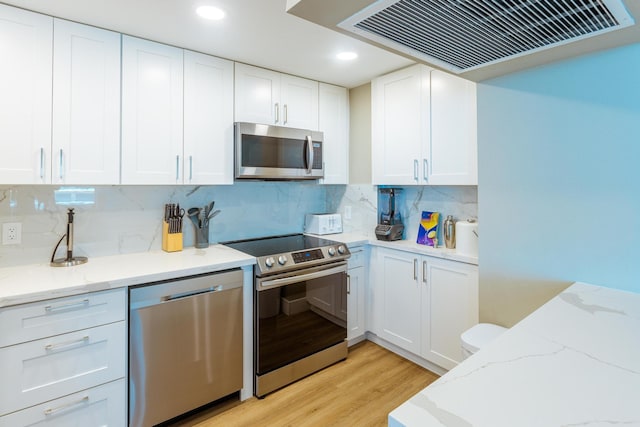 kitchen with white cabinets, appliances with stainless steel finishes, ventilation hood, and tasteful backsplash