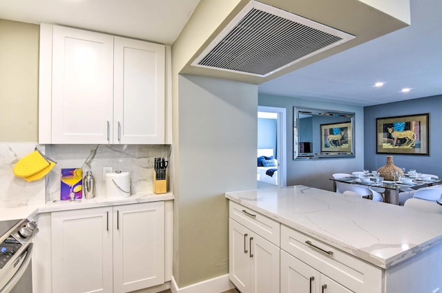 kitchen with white cabinets, backsplash, stainless steel stove, and kitchen peninsula