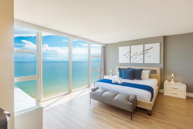 bedroom with access to outside, a water view, light hardwood / wood-style flooring, and floor to ceiling windows