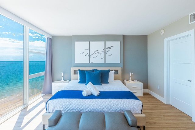 bedroom featuring a view of the beach, a water view, and light hardwood / wood-style flooring