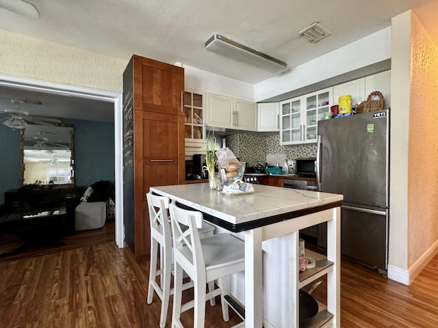 kitchen with white cabinetry, a center island, stainless steel refrigerator, hardwood / wood-style floors, and decorative backsplash