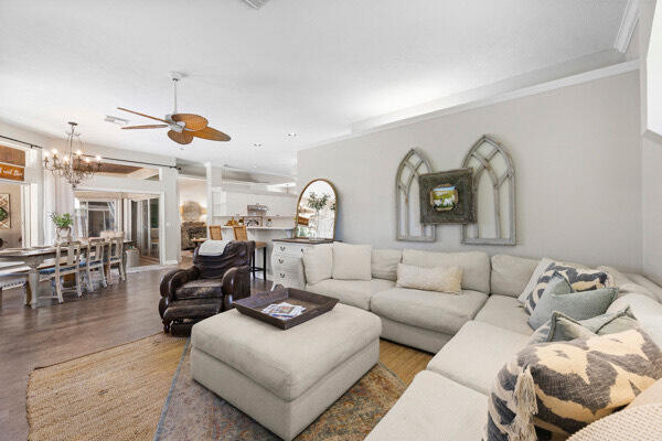 living room featuring wood-type flooring, ceiling fan with notable chandelier, and crown molding