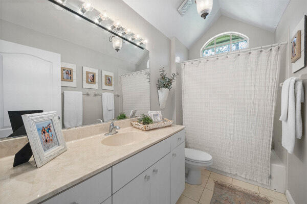 bathroom with tile patterned flooring, lofted ceiling, vanity, and toilet