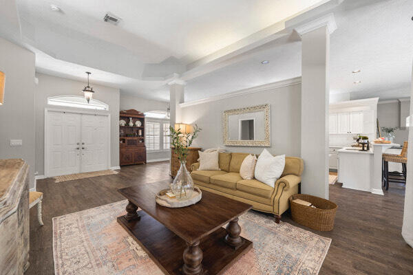 living room with a tray ceiling, decorative columns, and dark wood-type flooring