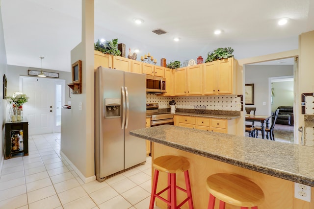 kitchen with appliances with stainless steel finishes, light tile patterned flooring, backsplash, a breakfast bar area, and light brown cabinets