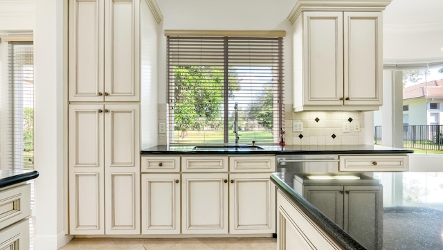 kitchen featuring backsplash, cream cabinets, sink, and dark stone counters