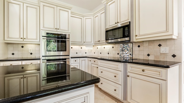 kitchen with tasteful backsplash, light tile patterned floors, dark stone counters, cream cabinetry, and stainless steel appliances