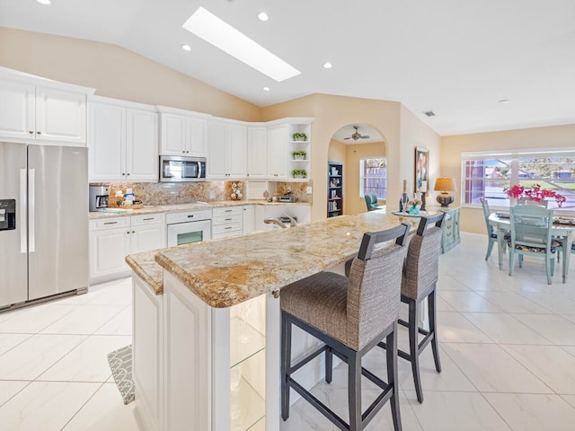 kitchen featuring appliances with stainless steel finishes, white cabinetry, a kitchen bar, vaulted ceiling, and light stone counters