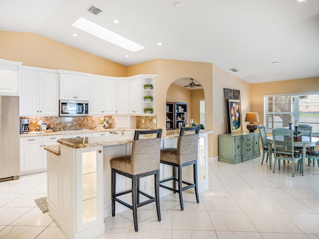 kitchen with white cabinetry, stainless steel appliances, light stone countertops, and an island with sink