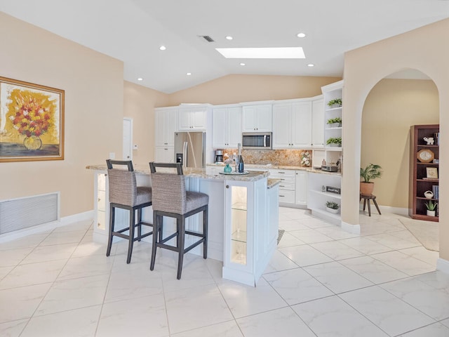 kitchen with a kitchen breakfast bar, an island with sink, stainless steel appliances, lofted ceiling with skylight, and white cabinets