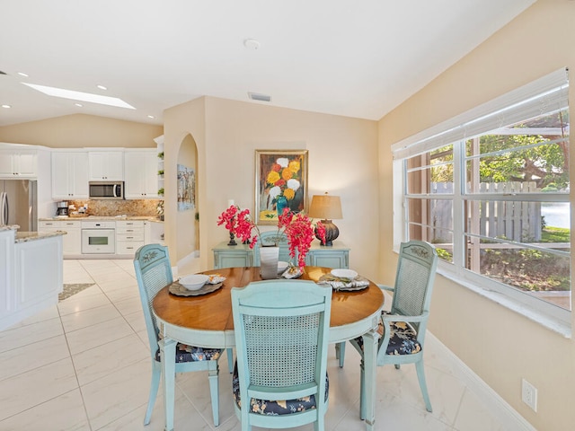 dining space with vaulted ceiling with skylight and light tile patterned floors