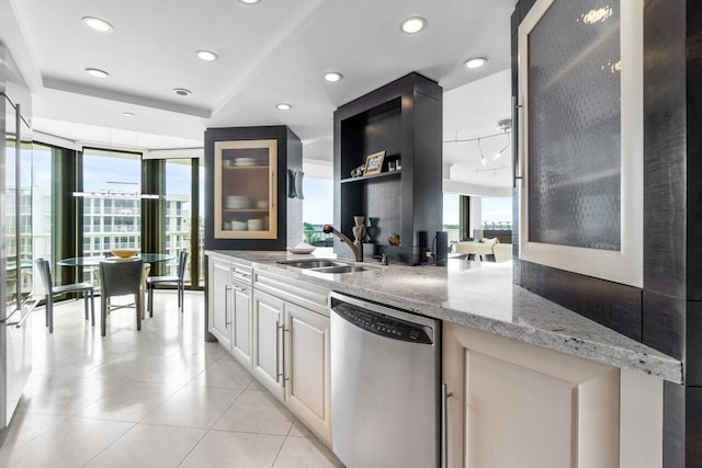 kitchen with light tile patterned floors, white cabinetry, light stone countertops, dishwasher, and sink