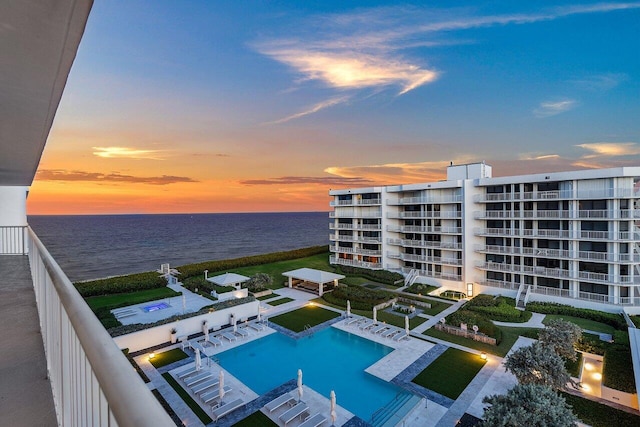 pool at dusk with a water view, a patio area, and a yard