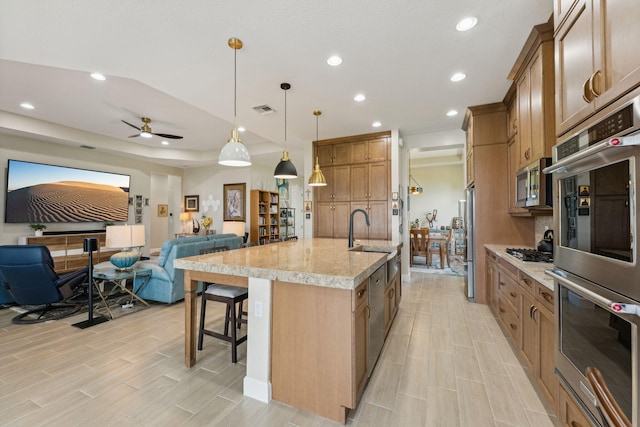 kitchen featuring ceiling fan, hanging light fixtures, stainless steel appliances, a breakfast bar, and a spacious island