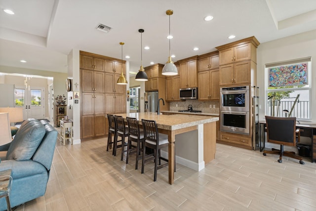 kitchen featuring pendant lighting, light hardwood / wood-style flooring, backsplash, stainless steel appliances, and a breakfast bar