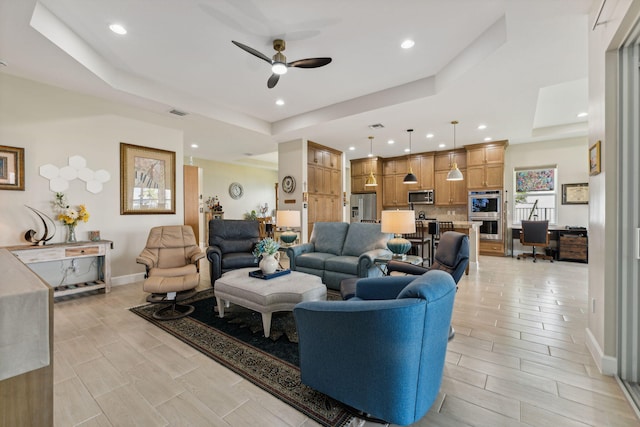 living room with a raised ceiling, light hardwood / wood-style floors, and ceiling fan