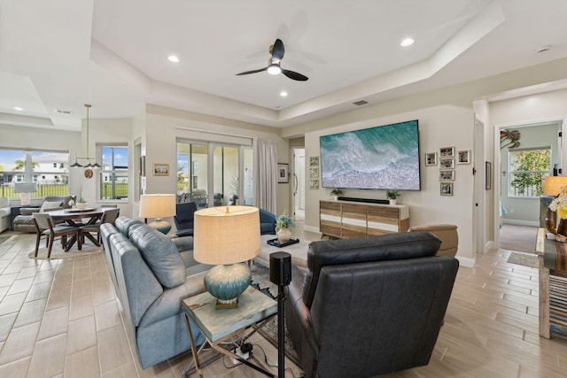 living room featuring a tray ceiling, ceiling fan, and plenty of natural light