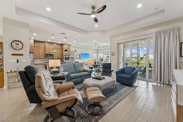 living room featuring light wood-type flooring, ceiling fan, and a raised ceiling