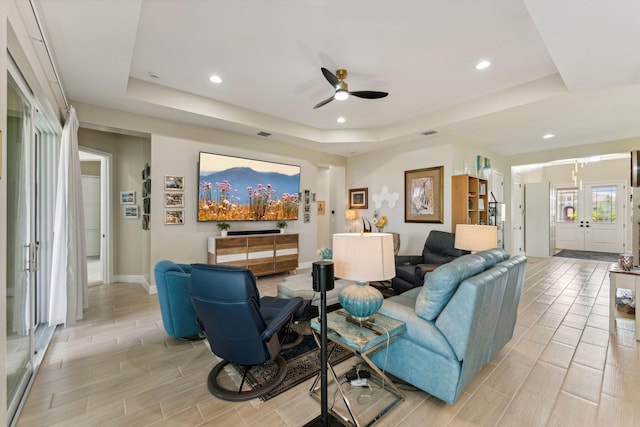 living room with a raised ceiling, ceiling fan, and light hardwood / wood-style flooring