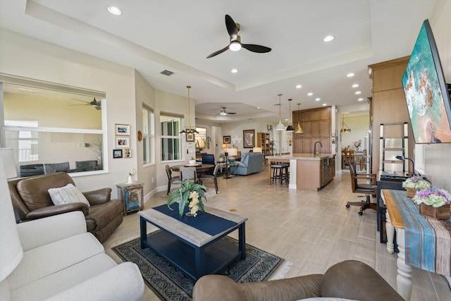 living room with light hardwood / wood-style flooring, ceiling fan, a raised ceiling, and sink