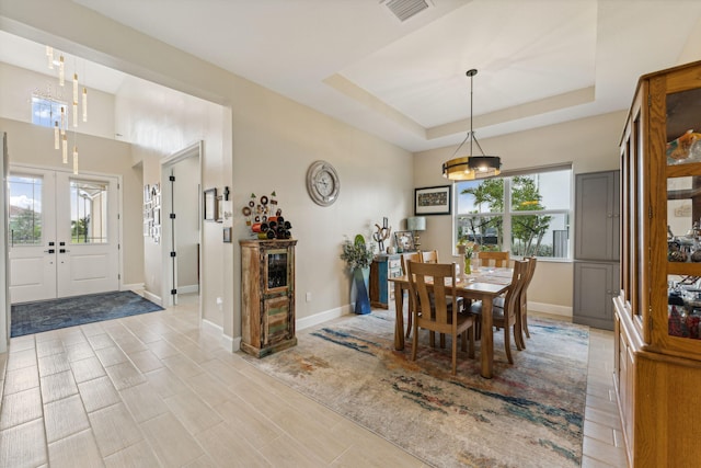 dining room featuring french doors, a raised ceiling, and light wood-type flooring