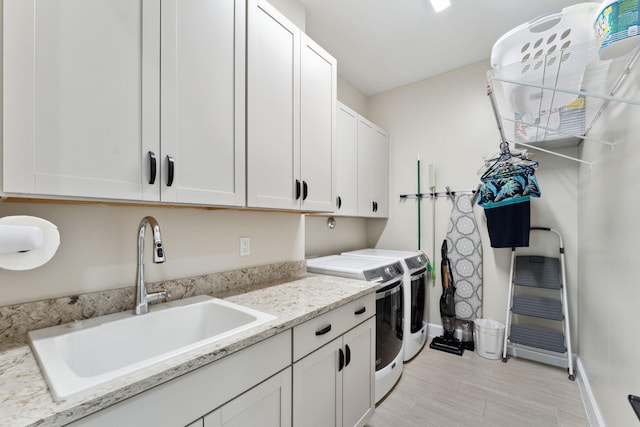 clothes washing area with washing machine and clothes dryer, light hardwood / wood-style floors, cabinets, and sink