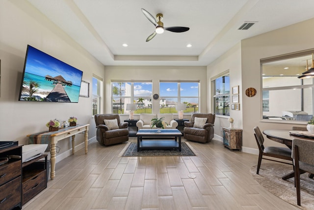 living room with ceiling fan, a raised ceiling, and light hardwood / wood-style floors