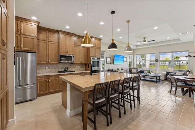 kitchen with ceiling fan, an island with sink, decorative light fixtures, appliances with stainless steel finishes, and a kitchen bar