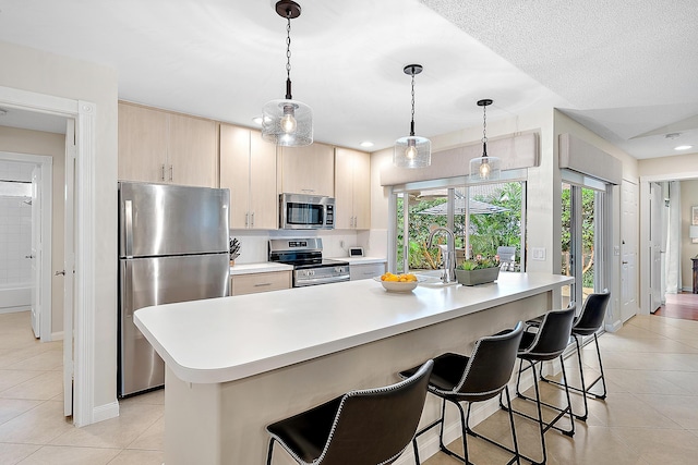 kitchen with a kitchen island with sink, a kitchen bar, stainless steel appliances, and light brown cabinetry