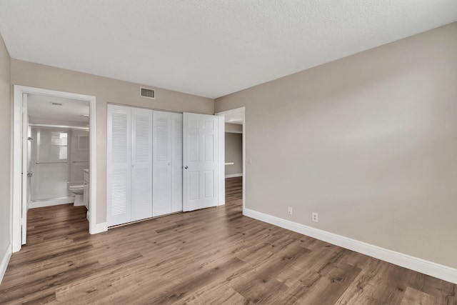 unfurnished bedroom with a closet, ensuite bathroom, wood-type flooring, and a textured ceiling