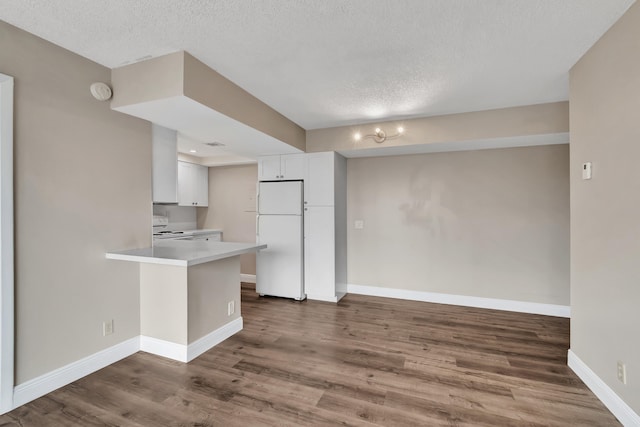 kitchen featuring dark wood-type flooring, kitchen peninsula, white cabinets, a textured ceiling, and white appliances