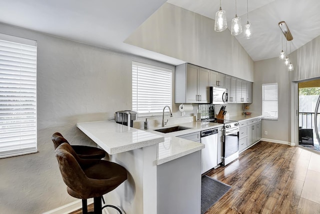 kitchen with a kitchen breakfast bar, appliances with stainless steel finishes, kitchen peninsula, decorative light fixtures, and sink