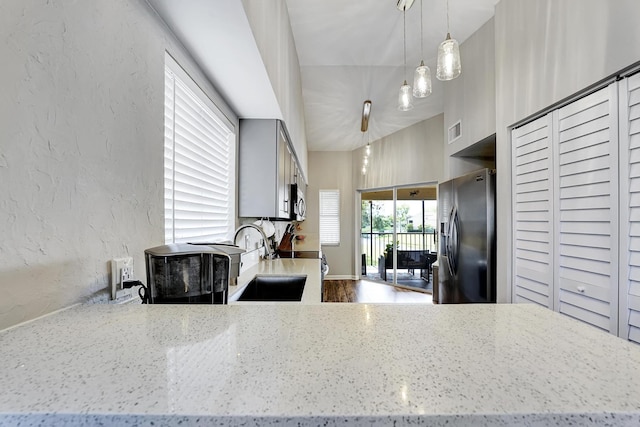 kitchen with hanging light fixtures, light stone countertops, stainless steel appliances, hardwood / wood-style flooring, and sink