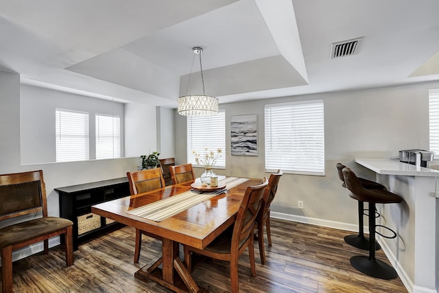 dining room featuring a healthy amount of sunlight, an inviting chandelier, a raised ceiling, and dark wood-type flooring