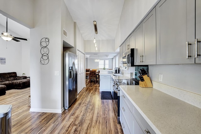 kitchen with hanging light fixtures, sink, wood-type flooring, high vaulted ceiling, and appliances with stainless steel finishes