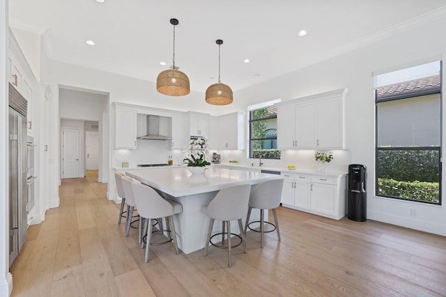 kitchen with white cabinetry, a kitchen island, light hardwood / wood-style floors, and wall chimney range hood