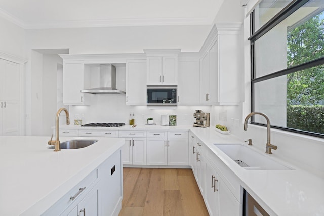 kitchen with white cabinets, wall chimney range hood, sink, and black microwave