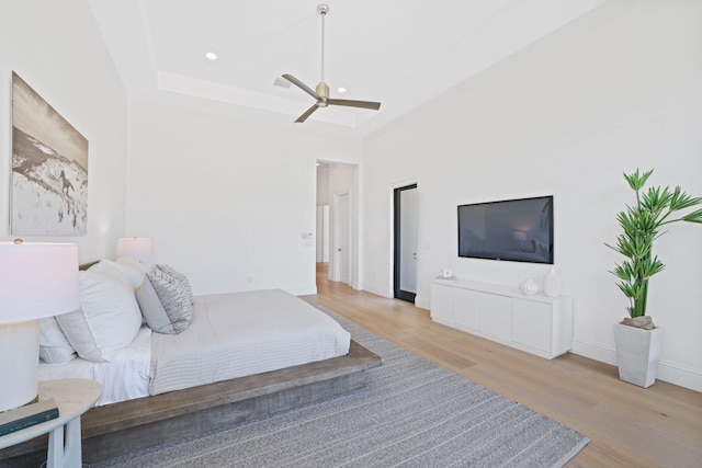 bedroom featuring ceiling fan, light hardwood / wood-style floors, and a raised ceiling